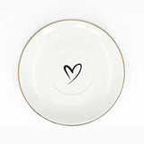 A white saucer with gold rim and a heart on the middle of the saucer.