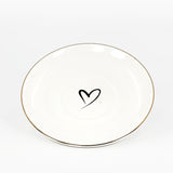 A white saucer with gold rim and a heart on the middle of the saucer.